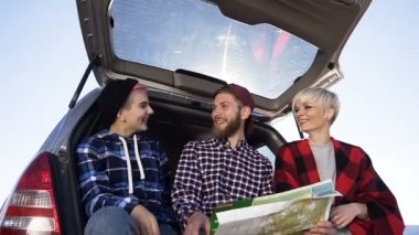 Bir harita ve mutlu neşeli görünümlü bir araba bagajında oturan genç Hipster arkadaşlar eğlenceli. Eğlenceli gezi ve doğa güzel Mekanlar
