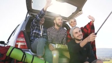 Selfie smartphone cep telefonu ile yapıyorsun, suv arabanın dağ zemin zemin üzerine eğilerek oturan neşeli arkadaş grubu. Tatil seyahat araba suv, doğa, dağlar, kavramı