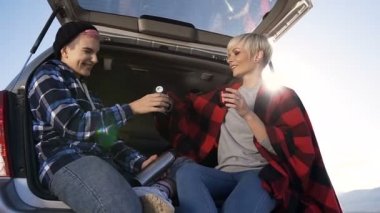 Termos ve içme kahve, kakao veya çay, konuşurken, holding araba bagajında oturan maceracı genç kadınlar açık havada doğa üzerinde gülüyor. Atış, ağır çekim dolly