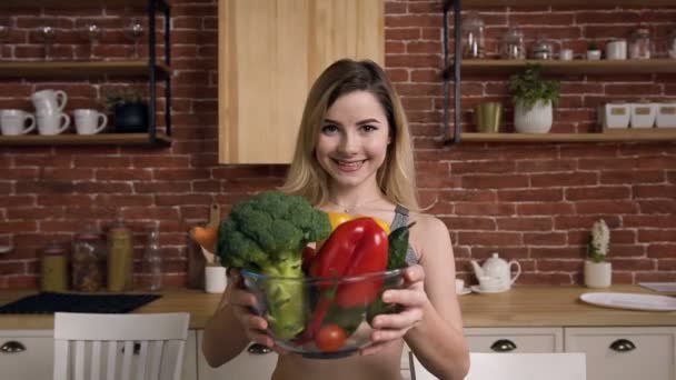 Porträt eines lächelnden, fitten Mädchens, das das Gericht mit Gemüse anbietet. — Stockvideo