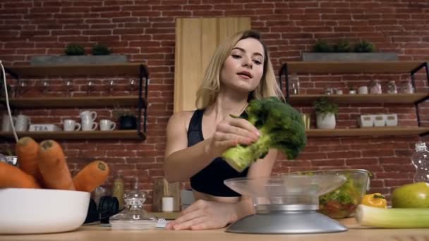 Мила молода жінка бере броколі і наносить на шкалу, щоб зважити її під час приготування їжі . — стокове відео