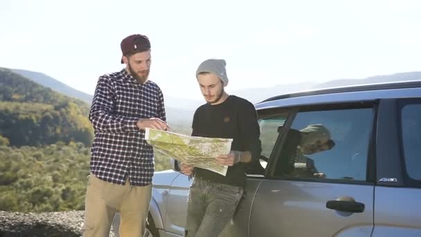 Двое друзей-хипстеров, которые ищут правильный путь, глядя на карту, стоящую возле машины на улице. Долли выстрелил — стоковое видео
