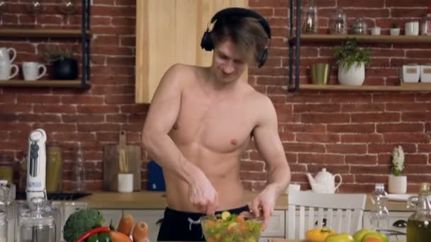 Bellissimo giovane uomo che ascolta musica in cuffia mentre cucina . — Video Stock