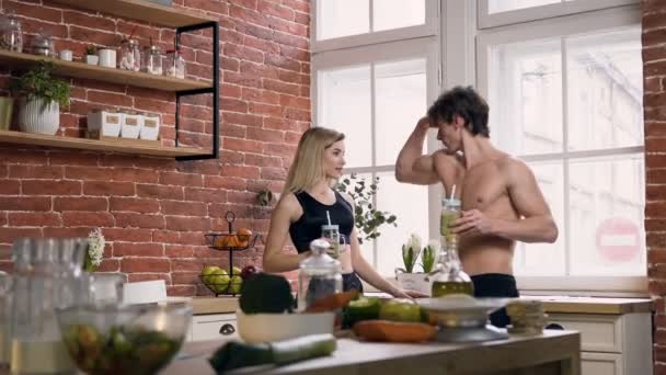 Handsome sport couple with smoothie in hands talking in the kitchen. — Stock Video