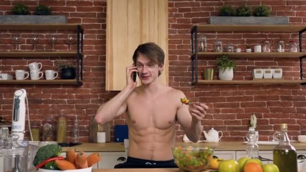 Bel homme en forme prendre le petit déjeuner tout en parlant avec un ami sur le téléphone intelligent dans la cuisine . — Video