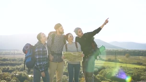 Groupe d'amis voyageurs caucasiens vérifient la carte en essayant de trouver le bon chemin sur le sommet de la montagne au coucher du soleil. Tourisme et mode de vie sain concept. Dolly shot — Video