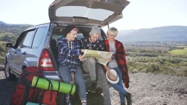 Mutlu üç arkadaş yol haritası gün batımında gülümsemeyle süre seyahat araba bagajı önünde oturma arıyoruz. Arkadaşlar bir yol gezisi bir haritaya bakıyordum Dağları'nın bir gövde arabanın içinden