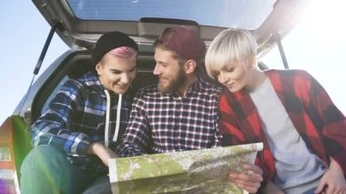 İki genç kadın ve bir adam arabanın bagajında otururken doğru yol aramak için Haritayı kullanarak kapatın.