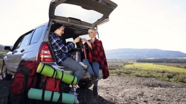 Dolly bardak çay tungur ve içme, arabanın güneş ışığı ile dağ zemin üzerine oturan iki sevimli kadın.