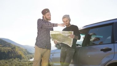 İki erkek şık arkadaş arıyor harita için yürüyüş ve dağ arka plan üzerinde taraftan.