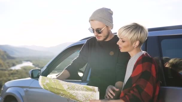 Atractiva pareja joven utilizando el mapa para elegir la dirección para la caminata en el fondo de la montaña . — Vídeos de Stock