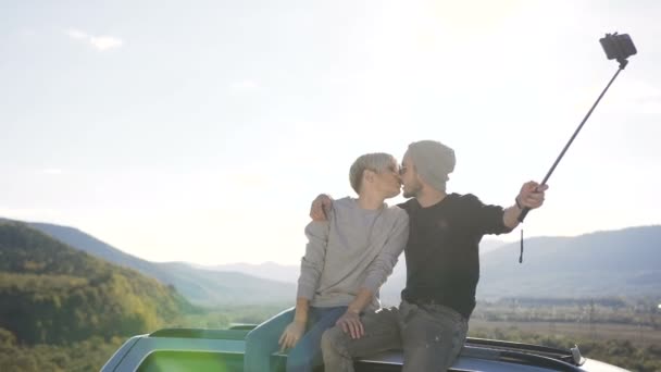 Ευτυχισμένο ζευγάρι κάθεται στην οροφή του αυτοκινήτου και possing της κάμερας έξυπνο τηλέφωνο στο βουνό. — Αρχείο Βίντεο