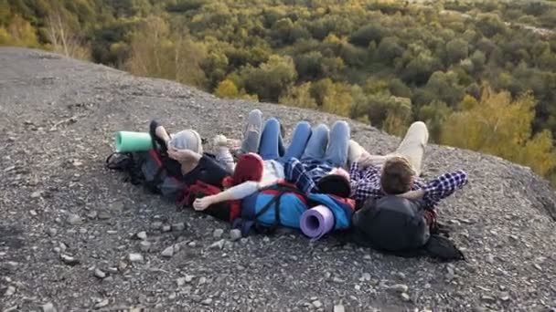 Quatre amis caucasiens couchés sur le sac à dos sur le sol dans la montagne . — Video