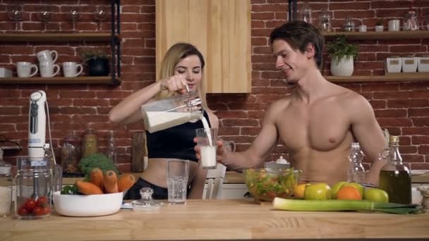 Familie paar heeft ontbijt in een gezellige keuken, jonge mooie vrouw giet melk haar vriendje of yoghurt in glas. Mensen, koken, gezonde voeding concept — Stockvideo