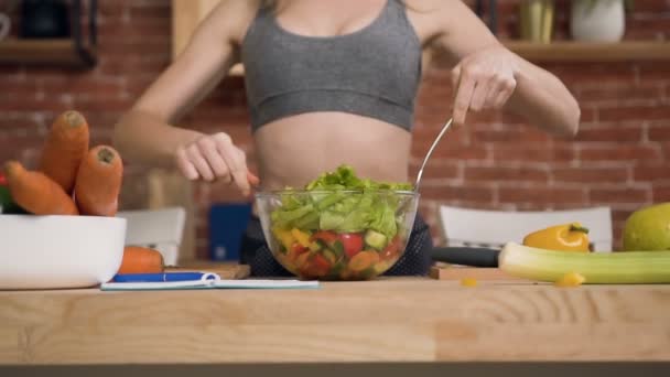 Mujer joven está preparando ensalada de verduras después del entrenamiento en la cocina en casa. Concepto de fitness y estilo de vida saludable — Vídeo de stock