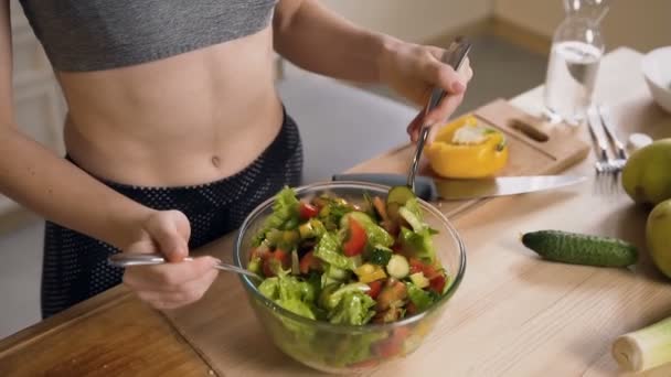 Genç kadın evde mutfakta egzersiz yaptıktan sonra zeytinyağı kullanarak taze yeşil sebzeler tarafından bir vegan salata hazırlanıyor. Fitness ve sağlıklı gıda konsepti. — Stok video