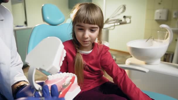 Küçük kız plastik modellerde diş fırçası kullanmayı öğretmek Afrika diş hekimi. — Stok video