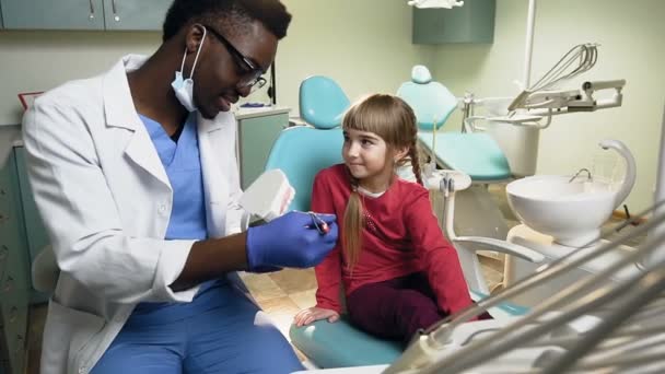 Afrikanska tandläkare visar hur man borstar tänderna på plast modell till ung kvinnlig patient. — Stockvideo