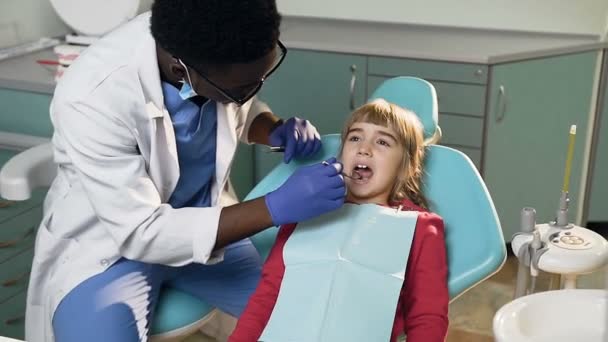 Dentista africano masculino tratando dientes de niña . — Vídeo de stock