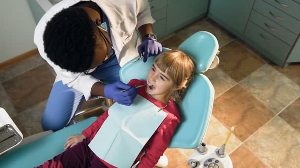 Dentista africano masculino verificando os dentes da menina . — Vídeo de Stock