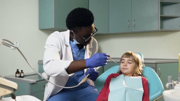 Africké mladý zubař dokončovací zkontrolovat zuby malou holčičku. — Stock video