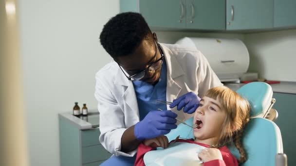 Jeune dentiste africain vérifiant les dents de la petite fille . — Video