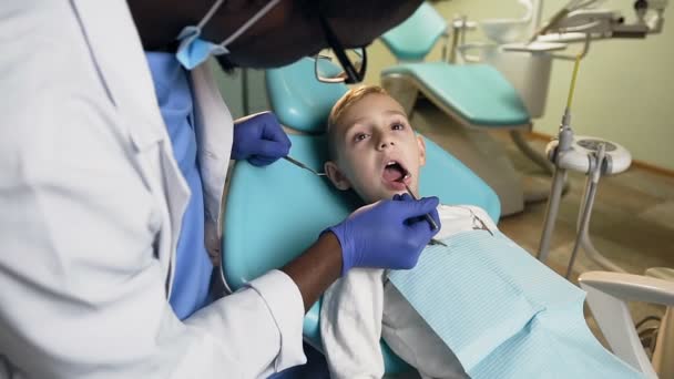 アフリカの男性歯科医が小さな男性患者の歯をチェック. — ストック動画