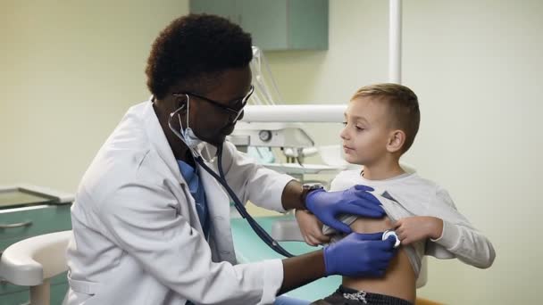 Pěkný africký lékař kontrolu malého chlapce v kanceláři nemocnice. — Stock video
