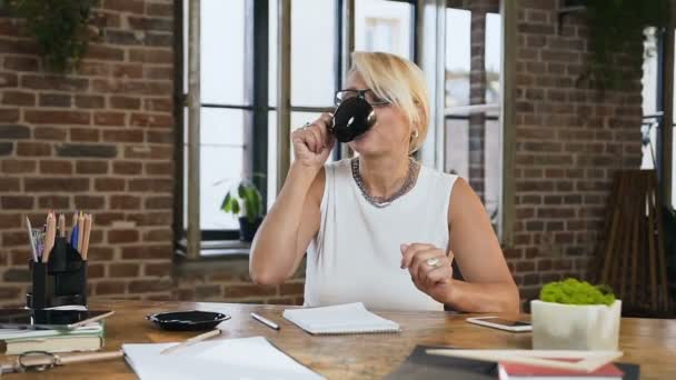 Aantrekkelijke vrouw is het controleren van rapportering in het dagboek terwijl drinken koffie zitten achter de balie in kantoor aan huis. Binnenshuis. Bedrijfsleven, onderwijs en mensen concept — Stockvideo