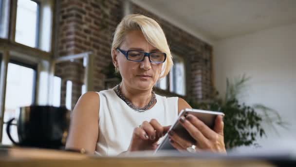 Mooie zakelijke vrouw zit aan een tafel controleert de mail op de tablet van de computer thuis op kantoor kamer — Stockvideo