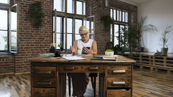 Atractiva mujer de negocios sentada en la mesa está escribiendo en la tableta durante el tiempo de trabajo en la oficina moderna — Vídeos de Stock