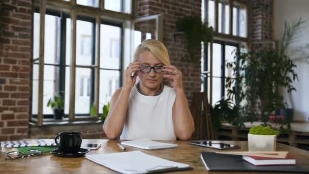Atraktivní Kavkazský žena s bolestí hlavy dokončí práci na stůl a odstraňuje brýle — Stock video