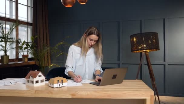 Gericht vrouwelijke architect bezig met het ontwerpen van toekomstige huis met behulp van blauwdruk, huis model en laptop. — Stockvideo