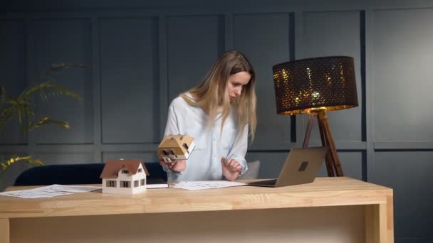 Νεαρός αρχιτέκτονας που εργάζεται με σχέδιο και σπίτι μοντέλο χρησιμοποιώντας φορητό υπολογιστή. — Αρχείο Βίντεο