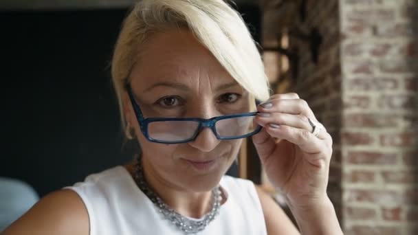 Retrato de Closeup de cara linda mulher de meia-idade colocando óculos sorrindo para a câmera, visão saudável. Indoor tiro — Vídeo de Stock