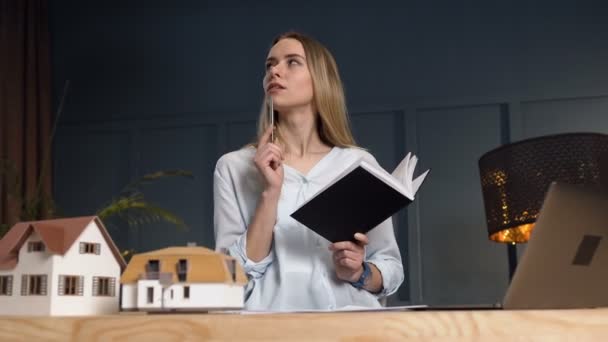 Pensativo agente inmobiliario femenino con cuaderno en las manos durante el trabajo en la oficina . — Vídeos de Stock