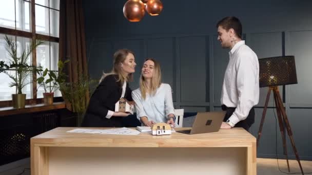 Mujer joven arquitecta trabajando en la construcción de planos mientras viene sus dos compañeros de trabajo y empezar a discutir ideas de diseño . — Vídeo de stock