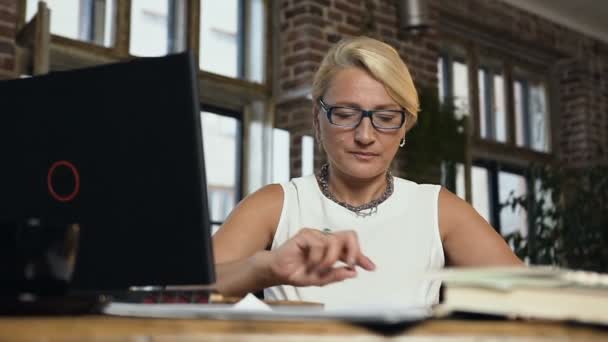 Retrato de la mujer de negocios caucásica de mediana edad está utilizando el portátil para escribir algo en el cuaderno de notas mientras trabaja en la oficina — Vídeos de Stock