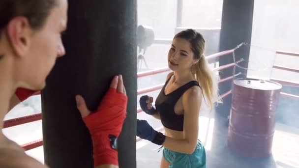 Focused man holding punching bag while attractive woman hitting it. — Stock Video