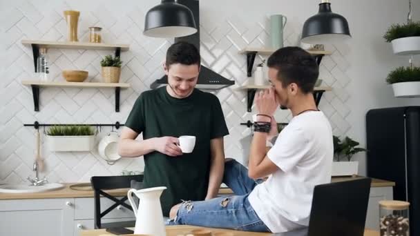 Pareja gay masculina divertida está bebiendo su café de la mañana mientras está de pie en la cocina en casa. Gente, homosexualidad, familia del mismo sexo, concepto de relaciones homosexuales — Vídeos de Stock