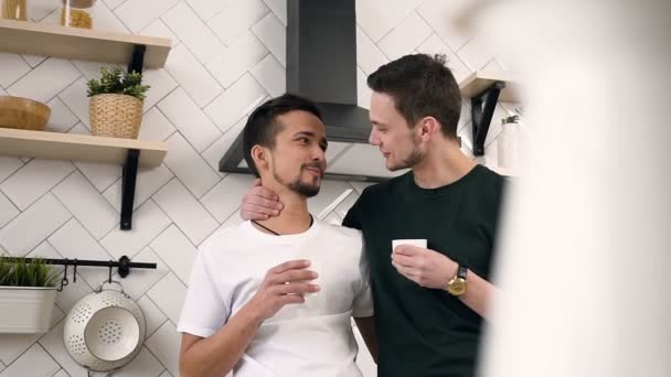 Giovane coppia gay maschile che si abbraccia bevendo caffè mattutino mentre si trova in cucina a casa. Concetto di relazioni gay — Video Stock