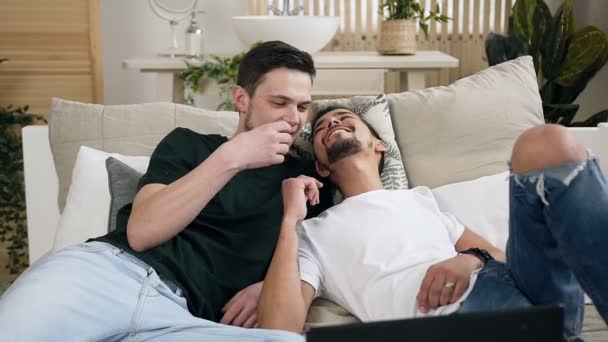 Aantrekkelijke homopaar liggen en knuffelen met behulp van laptop samen met gelukkige emotie in het bed op de slaapkamer. Gay mannen doorbrengen vakantie samen — Stockvideo