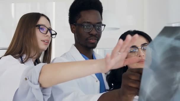 Portrait shot of three multi national doctors discussing xray of lungs of the patient during work day. — Stock Video