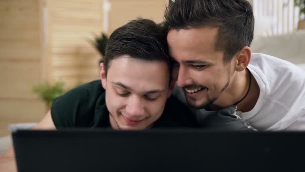 Portret van een jonge homo paar kijken laptop scherm in woonkamer, liggend op de Bank. Mooie jonge homo paar laptop gebruiken terwijl je samen plezier liggend op bed in de slaapkamer — Stockvideo