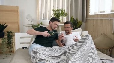 Yakışıklı bir eşcinsel adam onun ortağı kadehlerin içinde dökme köpüklü beyaz şarap yan yana ışık yatak odası, yatakta yatarken süre