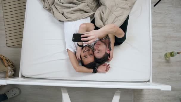 Homoseksuel par filme vlog mens liggende i en seng, vinke hænder, smile og tale med deres abonnenter, stille og roligt griner. Homosexul par mænd, der har munter stemning, mens de ligger i sengen og taler – Stock-video