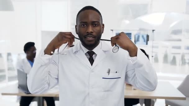 Close up shot of young male doctor putting stethoscope on the neck with team of staff on the background during conference. — Stock Video