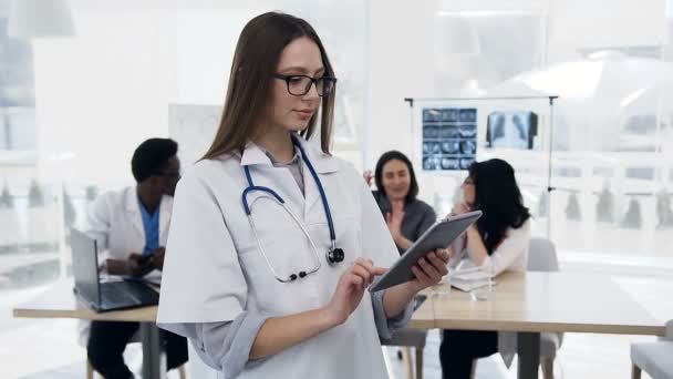 Schöne junge Frau mit Tablette mit Cowoker im Hintergrund in der Klinik. — Stockvideo