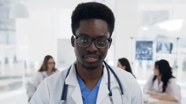 Portret pewnie Afryki lekarz mężczyzna podczas zespołu cowoker działa w tle, w szpitalu. — Wideo stockowe