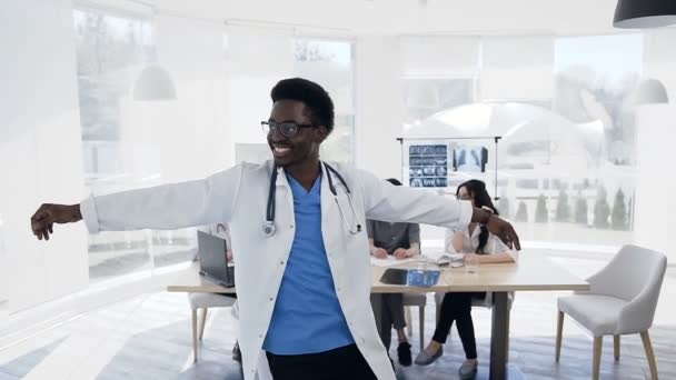 Щасливі африканських самця танці під час робочого дня з командою cowoker на фоні в лікарні. — стокове відео